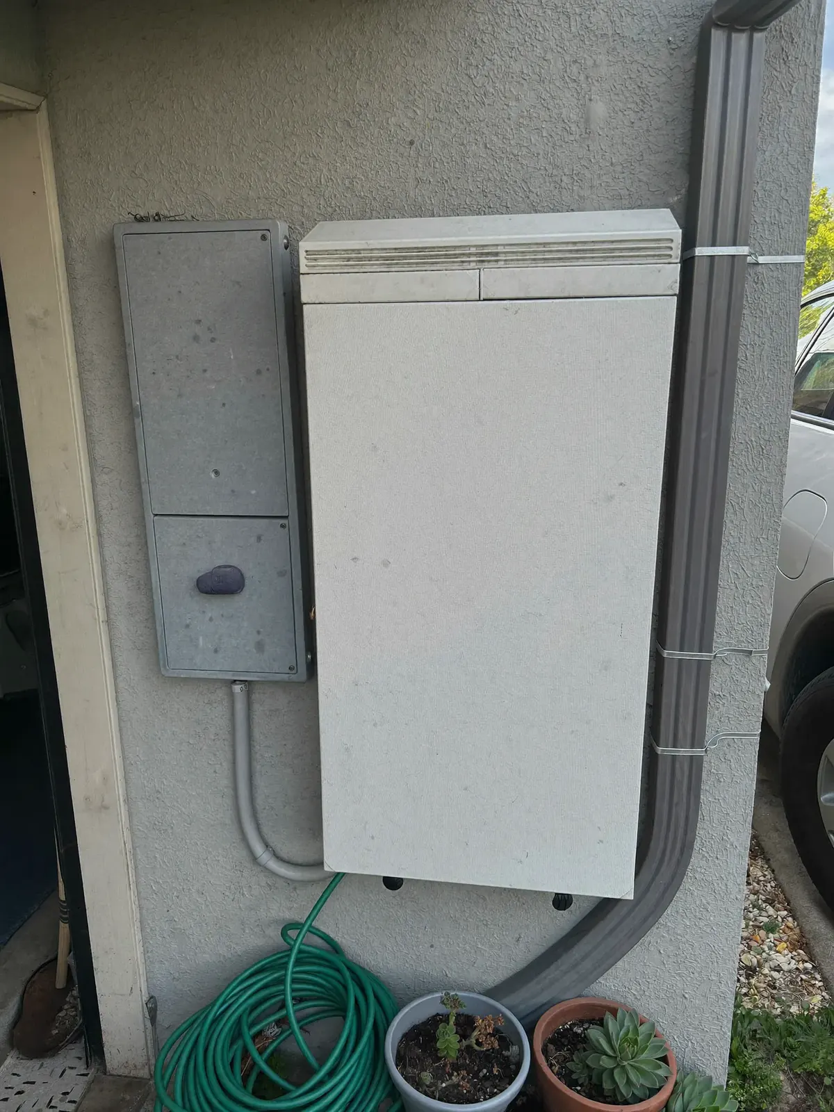 A plain white home battery mounted on a garage wall beside the electrical panel.