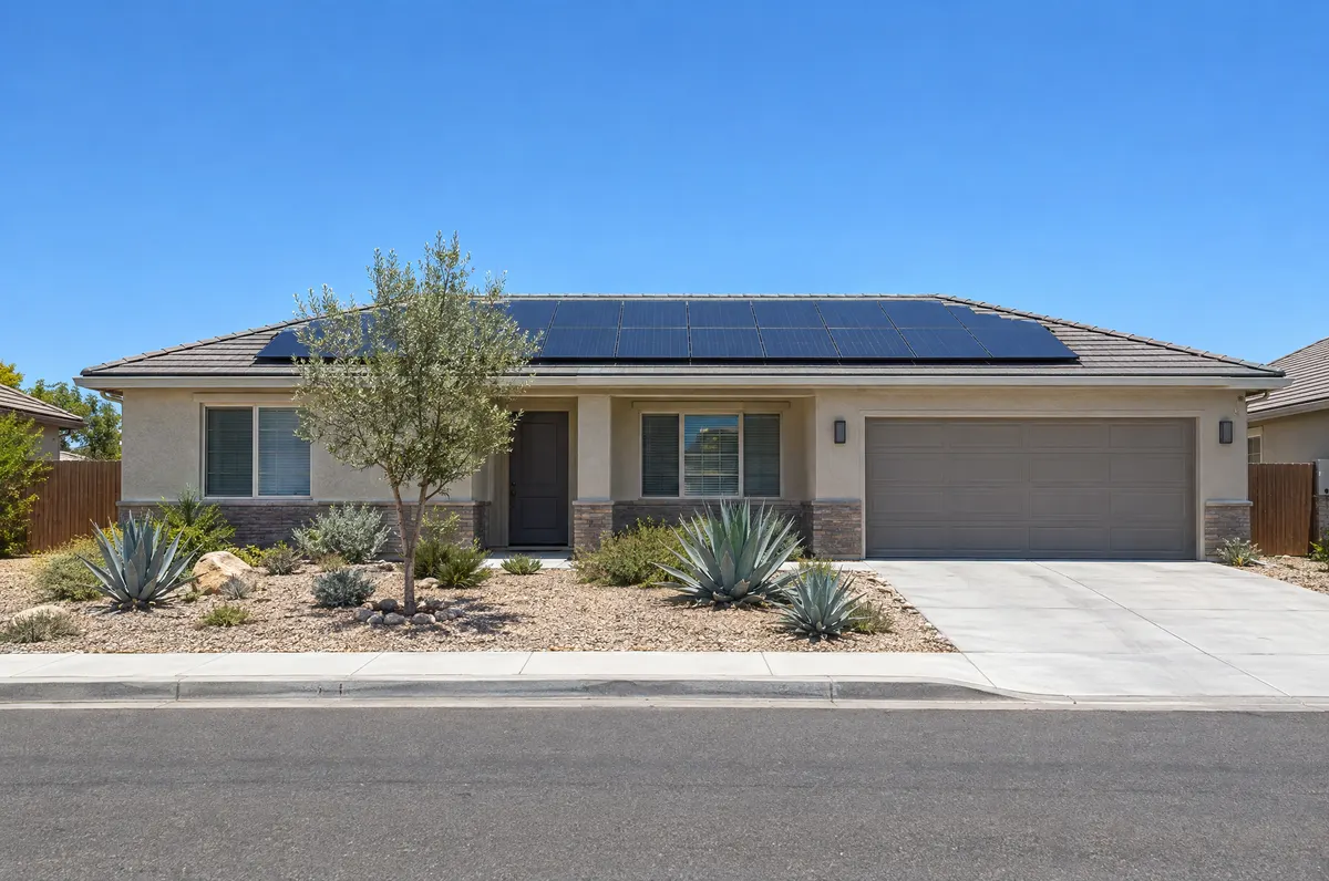 A single-story stucco home with solar panels on its roof on a sunny afternoon.