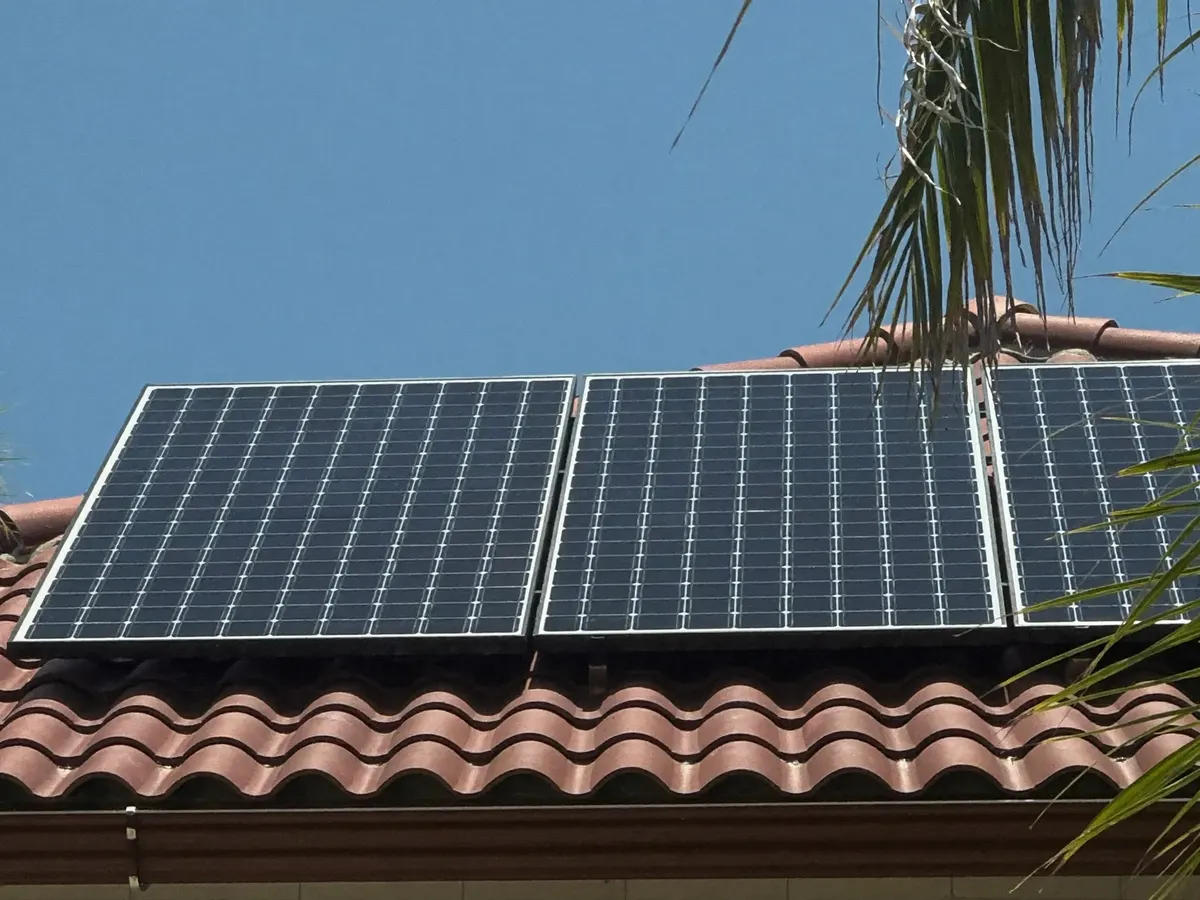 Black solar panels on a red clay tile roof under a blue sky.