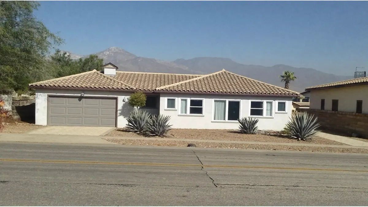 A single-story stucco ranch home with a tile roof and an agave yard, the San Gabriel mountains hazy behind it.